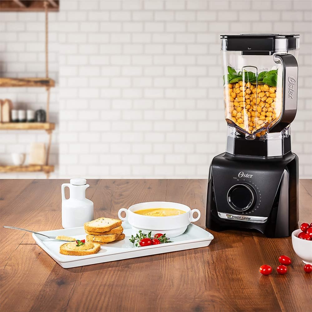 A sleek, modern Oster OLQ610 blender with a clear glass jar prominently displayed in the foreground, showcasing its elegant design and smooth lines. The blender's metal base gleams under soft ambient lighting, highlighting its metallic finish. In the middle ground, a kitchen countertop is visible, featuring fresh fruits and vegetables like bananas, strawberries, and spinach, suggesting its use for smoothies. In the background, a softly blurred kitchen environment with light wood cabinetry and subtle kitchenware creates a cozy, inviting atmosphere. The focus is sharp on the blender, emphasizing its high-quality build, while the soft bokeh adds a sense of warmth and practicality. The overall mood is functional and modern, perfect for showcasing usability and limitations. Liquidificador Oster OLQ610 Review Completo: Vale a Pena?